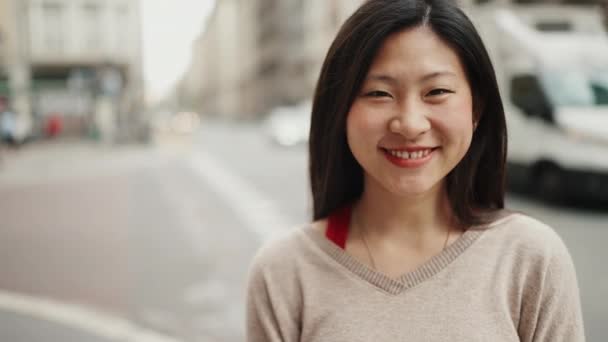 Portrét veselé asijské ženy, dívající se do kamery a usmívající se na ulici. Šťastná asijská dívka pózuje venku - Záběry, video
