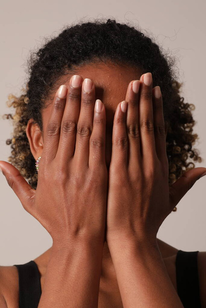 African American young woman is covering her face with her hands. Vertical shot. High quality photo. - Zdjęcie, obraz