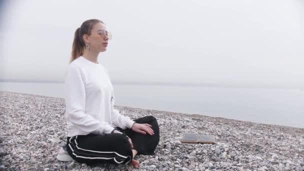 Kobieta siedzi na brzegu morza przy tablicy sadhu i ćwiczy oddychanie. Środek strzału - Materiał filmowy, wideo