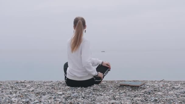 Una mujer inspirada se sienta en la orilla del mar en la posición de loto y se prepara para pisar la tabla de sadhu. Mid shot - Metraje, vídeo