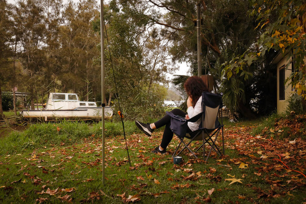 Vrouw zittend in kampstoel op caravanpark omringd door gevallen herfstbladeren, geen gezicht zichtbaar - Foto, afbeelding