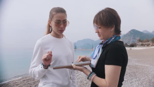 Zwei Frauen stehen am Ufer des Meeres - eine von ihnen hält Sadhu-Bretter und spricht darüber. Mittelschuss - Filmmaterial, Video