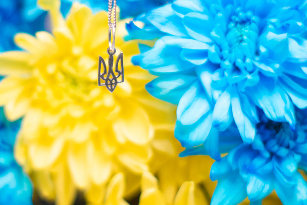 Tridente símbolo ucraniano en el fondo de los crisantemos azules y amarillos. Guerra en Ucrania 2022. Escudo de armas estatal de Ucrania. Símbolo de Ucrania - Foto, Imagen