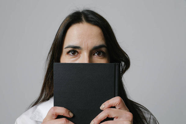 Middle-aged woman covering her face with her diary. Looking at the camera. High quality photo - 写真・画像