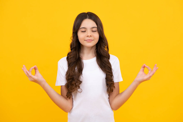 Niña adolescente 12-14 años en camisa blanca tomados de la mano en yoga om aum gesto relajarse meditar tratar de calma, aislado sobre fondo amarillo - Foto, imagen
