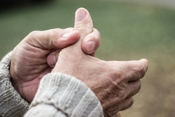 Starší muž trpí bolestí v prstech a rukou. Starý muž s bolestí prstů, pozadí bokeh, venku - Fotografie, Obrázek