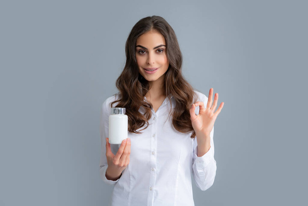 Woman with bottle pills. Young woman holding a vitamins isolated grey background. Young woman holding a vitamin. Vitamins and supplements, diet nutrition concept - Foto, afbeelding