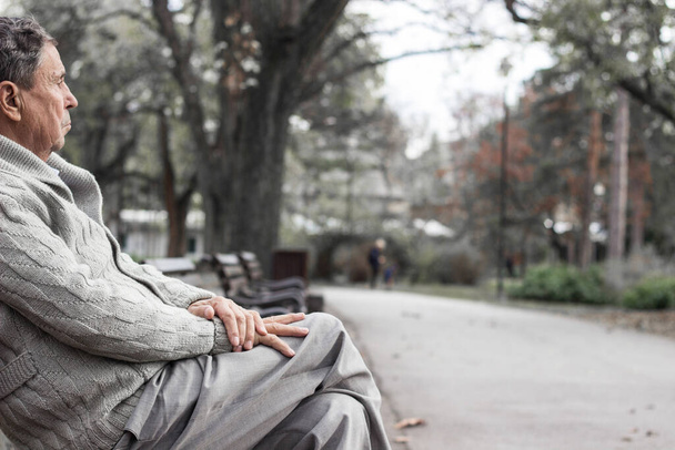 Ritratto di un anziano pensieroso seduto sulla panchina, nel parco pubblico, all'aperto. Vecchio che si rilassa all'aperto e distoglie lo sguardo. Ritratto di anziano in pensione - Foto, immagini
