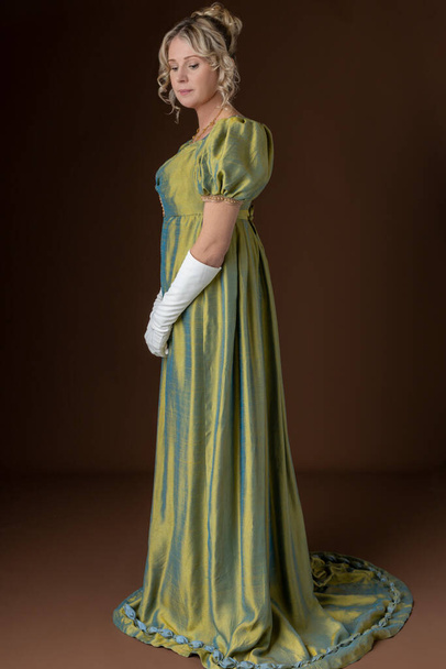 A blonde Regency woman wearing a green shot silk dress standing against a studio backdrop - Photo, Image