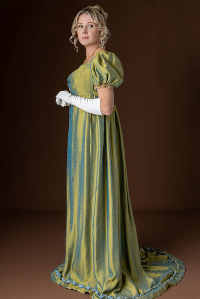 A blonde Regency woman wearing a green shot silk dress standing against a studio backdrop - Photo, image