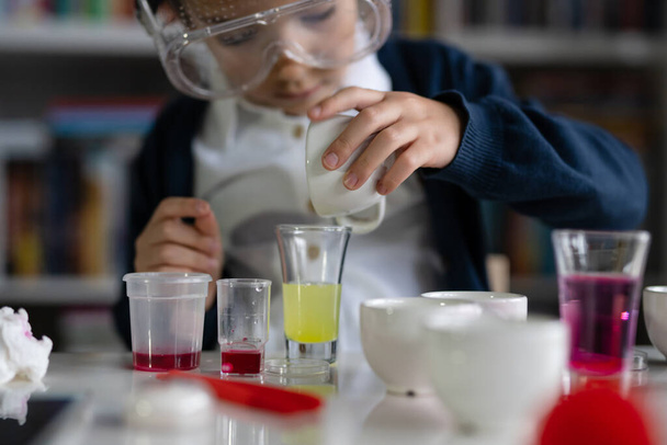 Close up on hand of One small caucasian boy scientist five years old sitting at the table playing with chemistry equipment toy preforming experiment learning and education concept front view - Foto, Bild