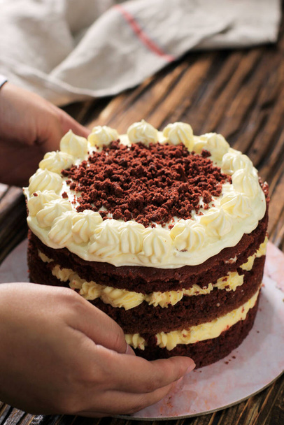 Целый красный бархатный торт со сливочным сыром глазурь и крошки, на сельском деревянном столе - Фото, изображение