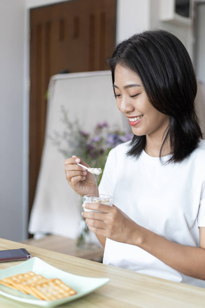 Pół-japońska kobieta je jogurt z płatkami zbożowymi na śniadanie w pokoju, Zdrowe jedzenie i utrzymanie układu pokarmowego, Najbardziej popularne i łatwe do jedzenia śniadanie żywności. - Zdjęcie, obraz