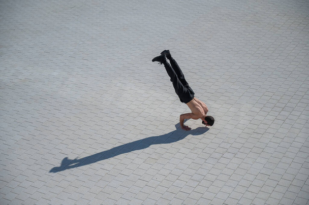 Shirtless man walks on his hands outdoors. View from above - Foto, imagen