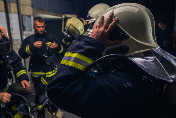 Grupo de bomberos de pie dentro de la brigada de bomberos con casco y uniforme de protección - Foto, Imagen