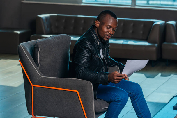 Porträt eines afroamerikanischen Geschäftsmannes, der in einem modernen Büro sitzt und mit seinen Kollegen über ein Projekt diskutiert - Foto, Bild