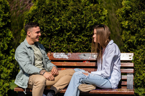 Twee vrienden praten en lachen zittend op de bank in een park - Foto, afbeelding