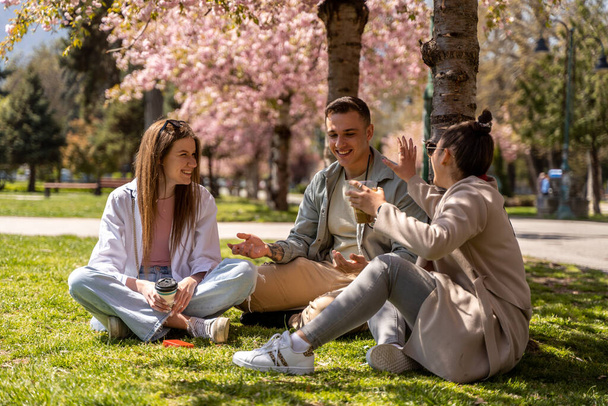 Groep van vrolijke vrienden wandelen buiten in de buurt van het meer en het drinken van koffie op mooie lente weer - Foto, afbeelding