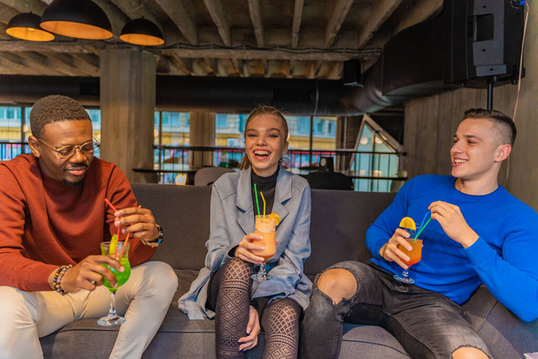 Tre amici multirazziali stanno bevendo le loro bevande mentre ridono insieme - Foto, immagini