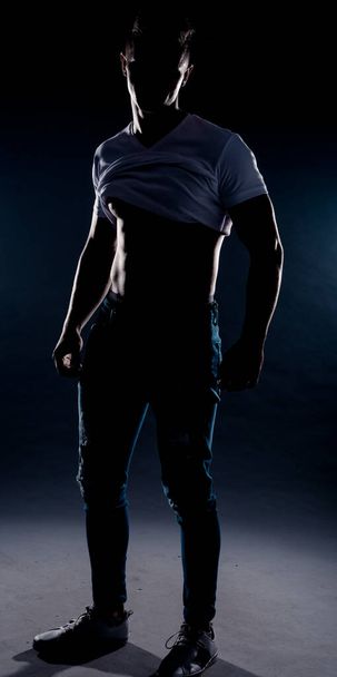 Atraktivní stylový muž pózující v modrých džínových kalhotách a bílém top - Fotografie, Obrázek