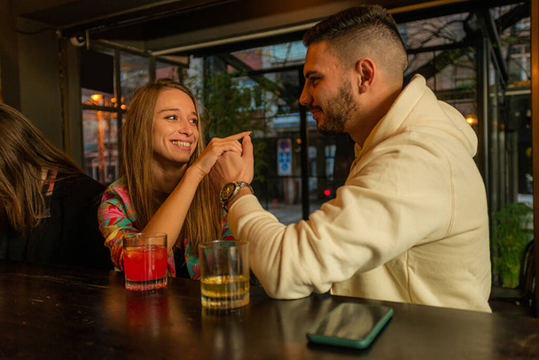 amazing and attractive young couple is talking and drinking while touching and sitting - Photo, Image