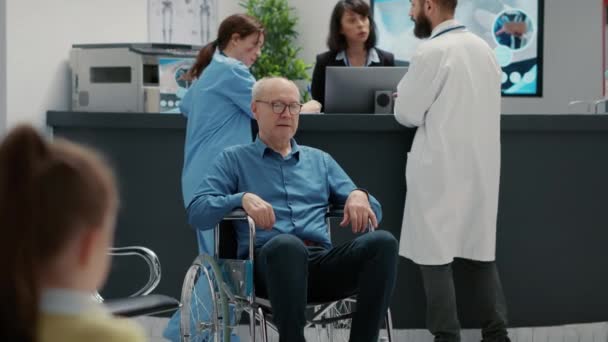 Vanhempi pyörätuolin käyttäjä istuu odotushuoneessa sairaalan vastaanotossa. Eläkkeellä oleva mies, jolla on vamma ja terveydentila ja joka käsittelee kroonista vammaa laitoksen aulassa. - Materiaali, video