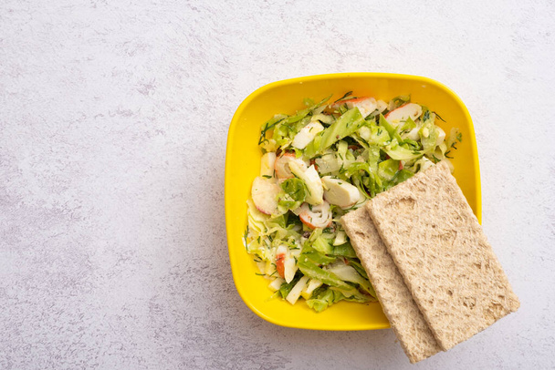 Pane dietetico e insalata di verdure fresche e bastoncini di granchio in un contenitore di plastica. Il concetto di alimentazione sana. - Foto, immagini