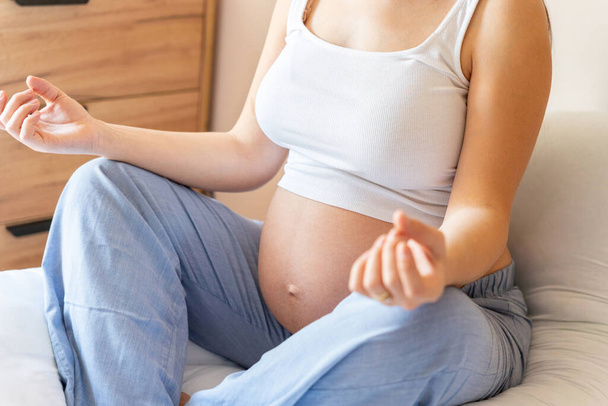 Διαλογισμός εγκυμοσύνης γιόγκα. Γιόγκα στο σπίτι. Όμορφη έγκυος γυναίκα διαλογίζεται ενώ κάθεται σε θέση λωτού. Έννοια μητρότητας, εγκυμοσύνης, τοκετού - Φωτογραφία, εικόνα