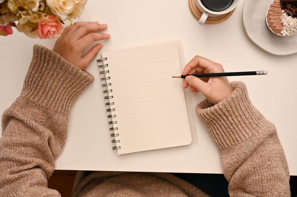 Egy főiskolás lány a munkaasztalán ír valamit a naplójába, vagy jegyzetel a jegyzetfüzetébe. felülnézet - Fotó, kép