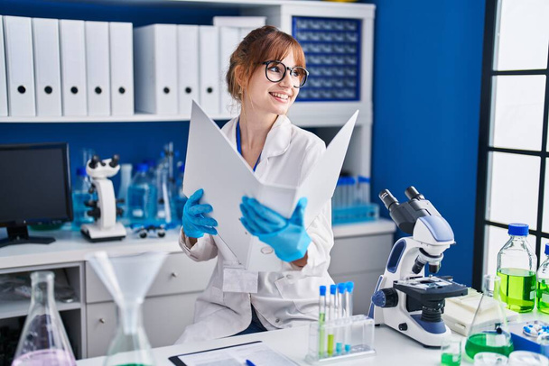 Młoda kobieta naukowiec uśmiecha się pewnie czytając raport w laboratorium - Zdjęcie, obraz