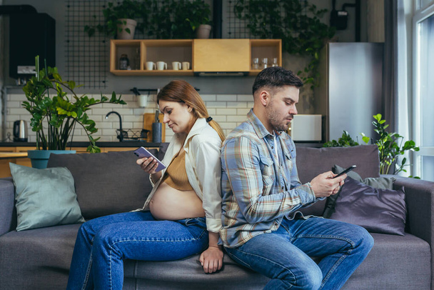 Family conflict and quarrel, husband and pregnant woman do not talk sitting on the couch with phones - Foto, immagini