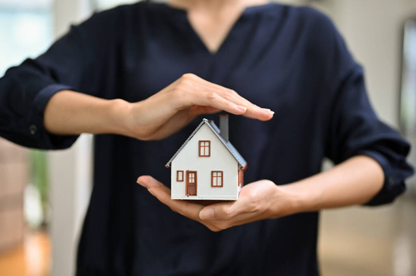 Property insurance and security concept. A female real estate realtor or house insurance agent making a protecting hands gesture over the house. cropped image - Photo, Image