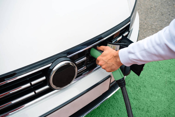 Closeup of unrecognizable man holding socket plugged into electric car outdoors - Photo, Image