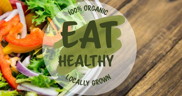 Image of eat healthy locally grown text in green, over bowl of fresh salad on wooden boards. vegan day, organic vegetable produce and healthy eating concept digitally generated image. - Foto, Imagem
