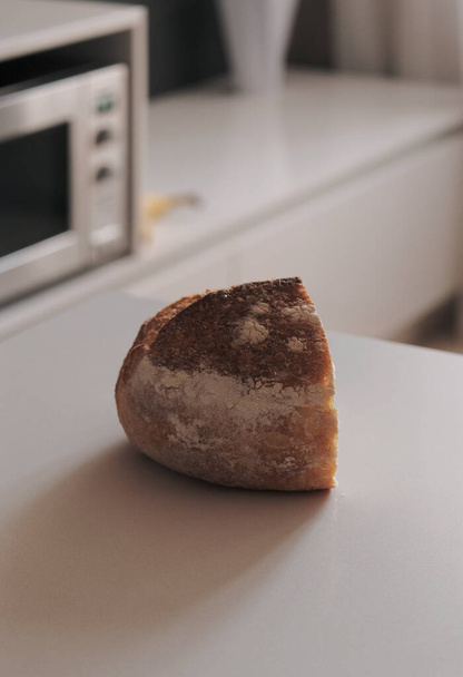 Polovina ručně vyrobeného chleba ležela na bílém stole v kuchyni. - Fotografie, Obrázek