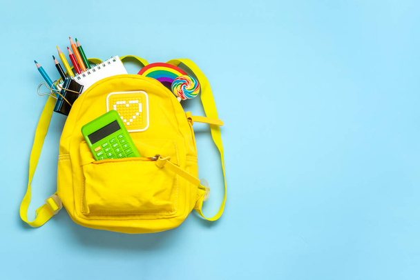 Back to school, education concept Yellow backpack with school supplies - notebook, pens, eraser rainbow, numbers isolated on blue background Top view Copy space Flat lay composition. - Photo, Image