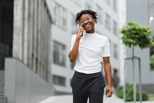 African business woman using smartphone while standing outdoors near office building. Concept of technology, work and modern lifestyles. Successful female career. - Photo, Image