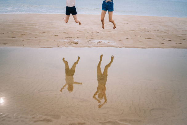 Счастливая девочка веселится на пляже, бегает и плещется на низкой воде, прыгая в воздух на морском побережье в солнечный день. Летние путешествия и отдых - Фото, изображение