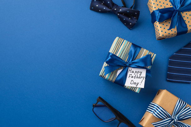 Concepto del Día del Padre. Foto vista superior de cajas de regalo con lazos de cinta postal azul corbata de lazo y gafas sobre fondo azul aislado - Foto, Imagen