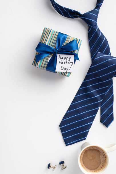 Concepto del Día del Padre. Vista superior vertical de la caja de regalo con lazo de cinta azul y gemelos de corbata azul postal y taza de café sobre fondo blanco aislado - Foto, Imagen