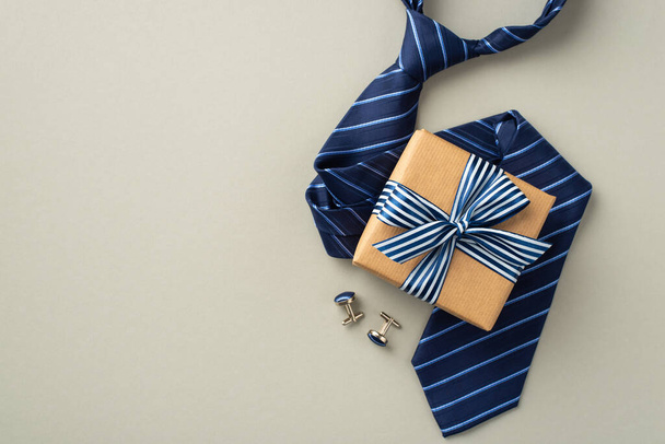 Concepto del Día del Padre. Foto de vista superior de la caja de regalo de papel artesanal con lazo de lazo a rayas azul corbata y gemelos sobre fondo gris pastel aislado - Foto, Imagen