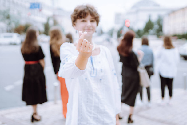 Koreanisches Symbol der Liebe mit zwei Fingern. Silhouette eines attraktiven Mädchens in ethnisch besticktem Hemd, ukrainische Frau, die ein Zeichen der Liebeserklärung zeigt, indem sie zwei Finger in Herzform faltet. Weicher Fokus, Unschärfe. - Foto, Bild