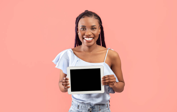 Kaunis nuori musta nainen tilalla tabletti tyhjä näyttö vaaleanpunainen studio tausta, mockup. Millennial Afrikkalainen Amerikan nainen osoittaa kosketuslevy näyttö malli verkkosivuilla tai uusi sovellus - Valokuva, kuva