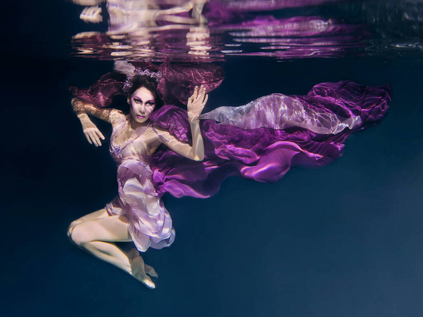 woman in colorful clothes on the dark background swimming underwater - Photo, Image