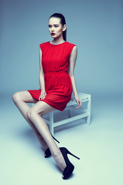 young elegant woman in red dress sit on stool, studio shot  - Фото, зображення