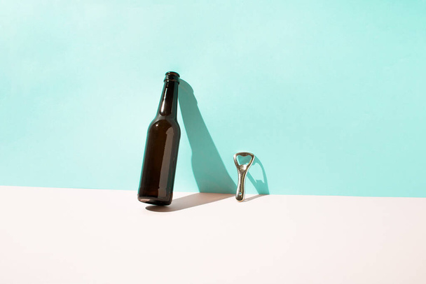 Garrafa de cerveja marrom e abridor de garrafa de metal encostado à parede com sombra afiada. Conceito mínimo de verão. - Foto, Imagem