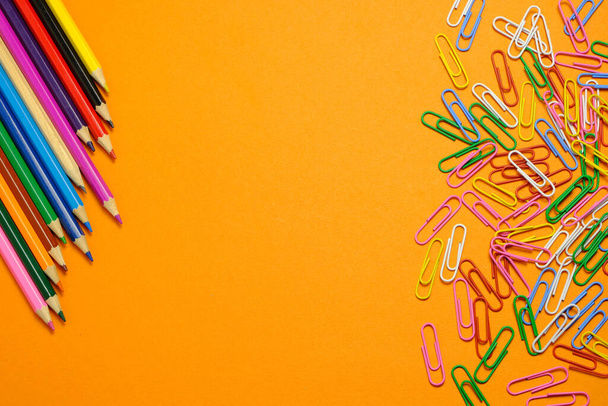 Colored pencils and stationery multi-colored paper clips on a orange background - Foto, Bild