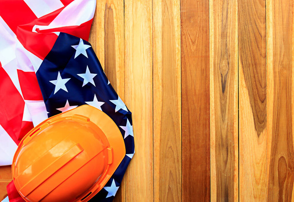 Pohled shora s oranžovou bezpečnostní přilbou a americkou vlajkou na pozadí dřevěného stolu. koncepce dne práce a dne nezávislosti. - Fotografie, Obrázek