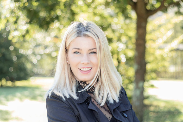 pretty smiling blonde woman looking at camera in a park - Fotografie, Obrázek