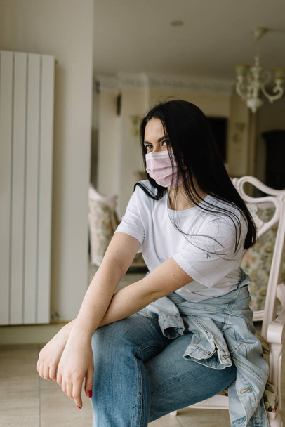 Quarantine. Stay at home for the quarantine prevention of the coronavirus pandemic. Sad girl in a protective medical mask sits and looks out the window. Epidemic and Coveid Prevention19. - Photo, image